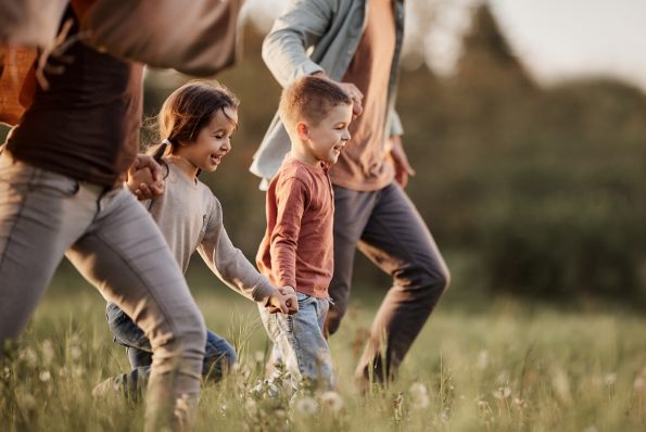 Happy siblings having fun while holding hands with their parents and running during spring day in nature. Copy space.
